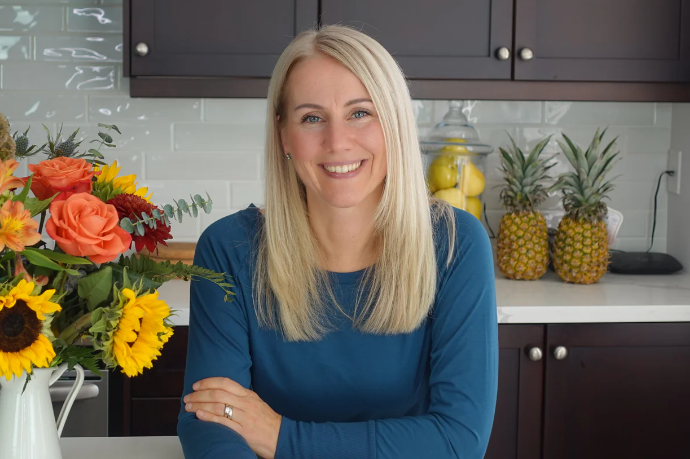 Eva in a blue shirt with her arms crossed sitting on a stool in a kitchen